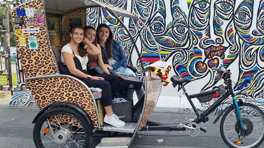 Women in rickshaw by colorful mural.