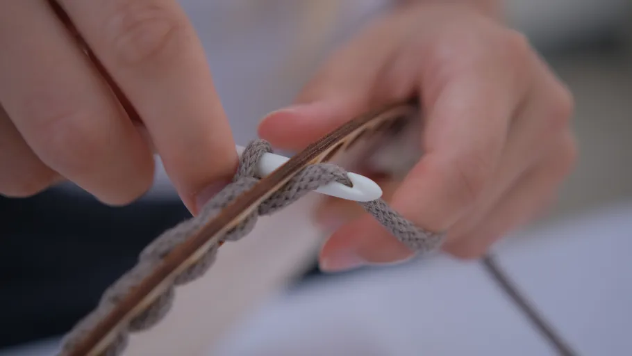 Hands weaving gray cord through a white button.