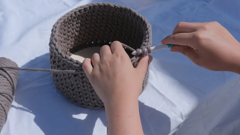 Hands crocheting gray basket outdoors.