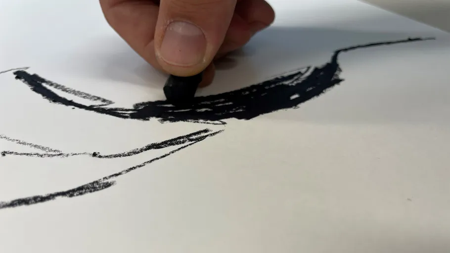 Hand zeichnet mit schwarzer Kreide auf Papier.