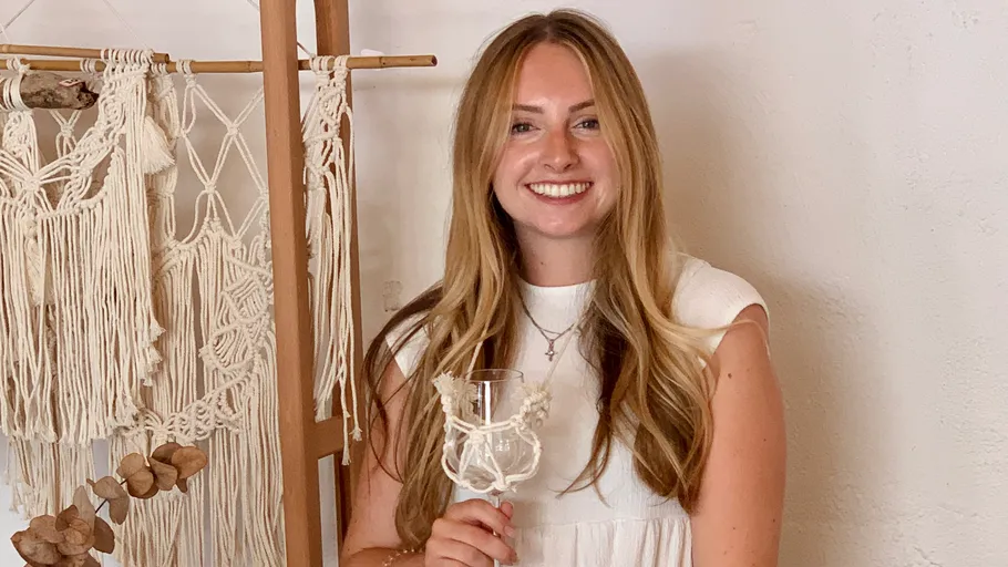 Woman smiling, holding a glass, macramé background.