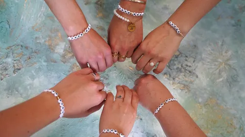 Sechs Hände mit personalisierten Armbändern bilden Kreis.