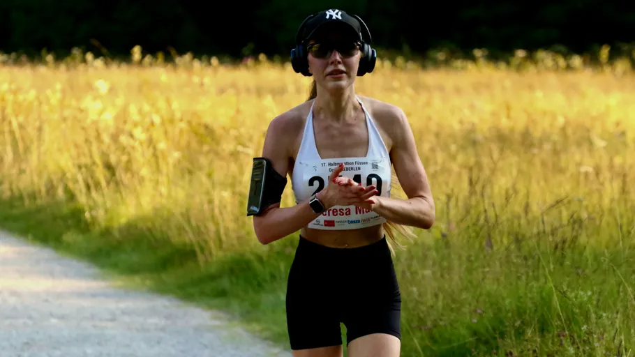 Runner wearing headphones on a grassy trail.
