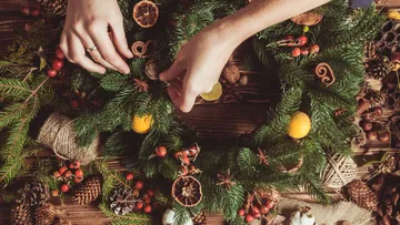 Hands decorating wreath on wooden table.