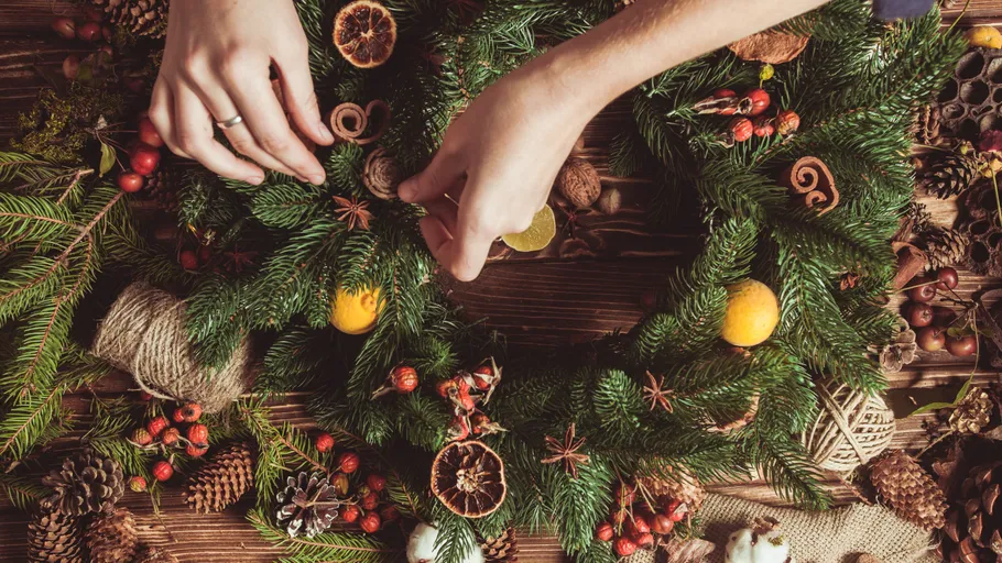 Hands decorating wreath on wooden table.