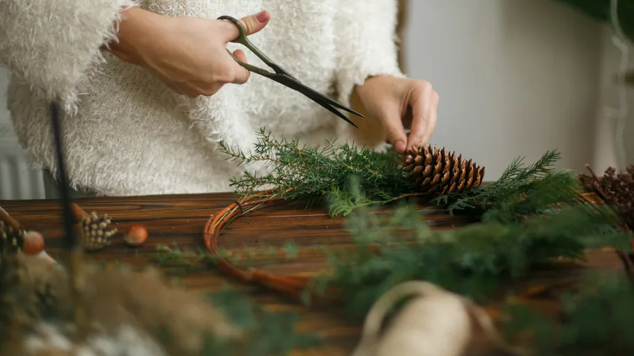 Person crafting wreath with pinecones on table.