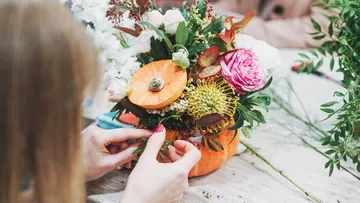 Person arranging flowers in pumpkin vase.