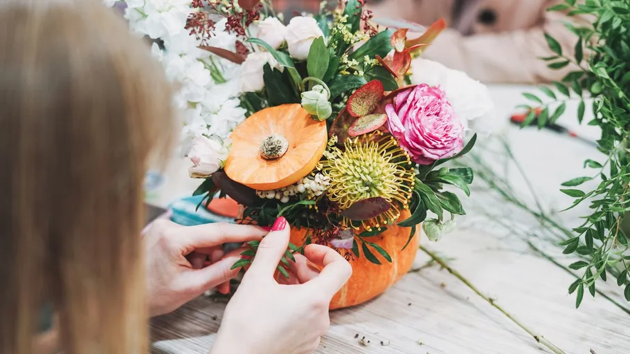 Person arranging flowers in pumpkin vase.