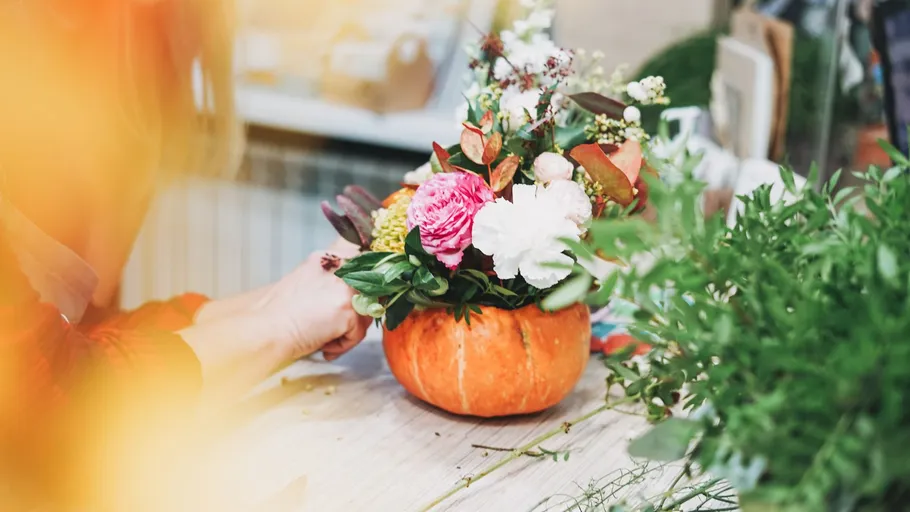 Person arranging flowers in pumpkin vase indoors.