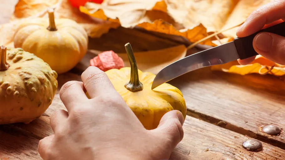 Person carving small pumpkin on wood table.