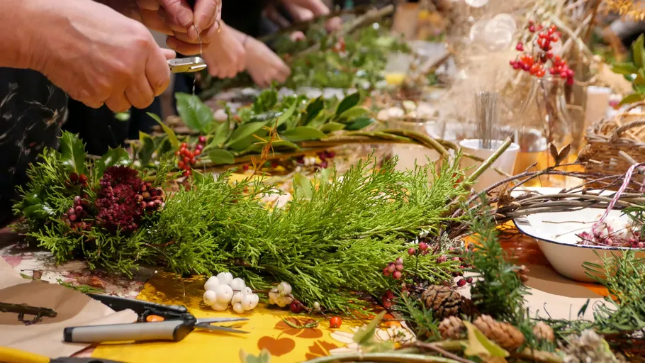 Hands crafting wreaths with greenery and berries.