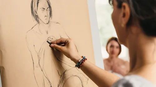Person drawing on easel, model in background.
