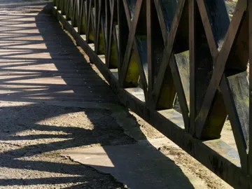 Wooden bridge casts shadows on the concrete path below.