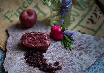 Rohes Fleischstück liegt auf Steinplatte, umgeben von Obst und Blumen.