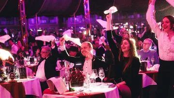 Menschen schwenken Servietten bei festlicher Veranstaltung.