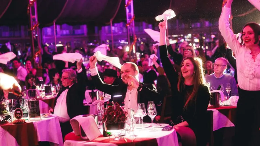 Menschen schwenken Servietten bei festlicher Veranstaltung.