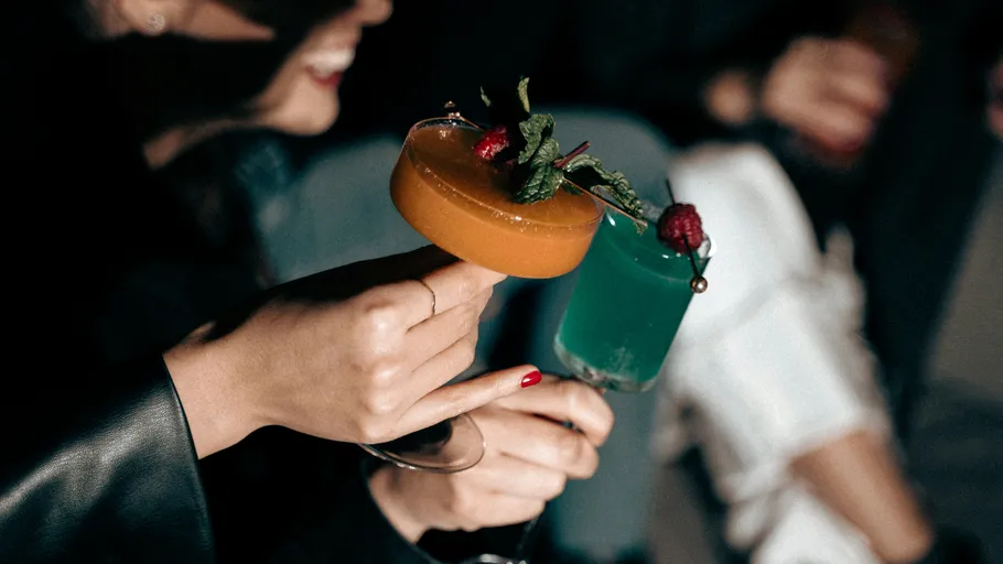 Hands holding colorful cocktails with garnish.