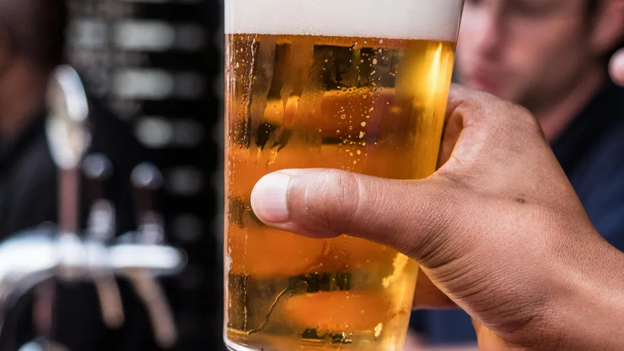 Hand holding a glass of beer, blurred background.