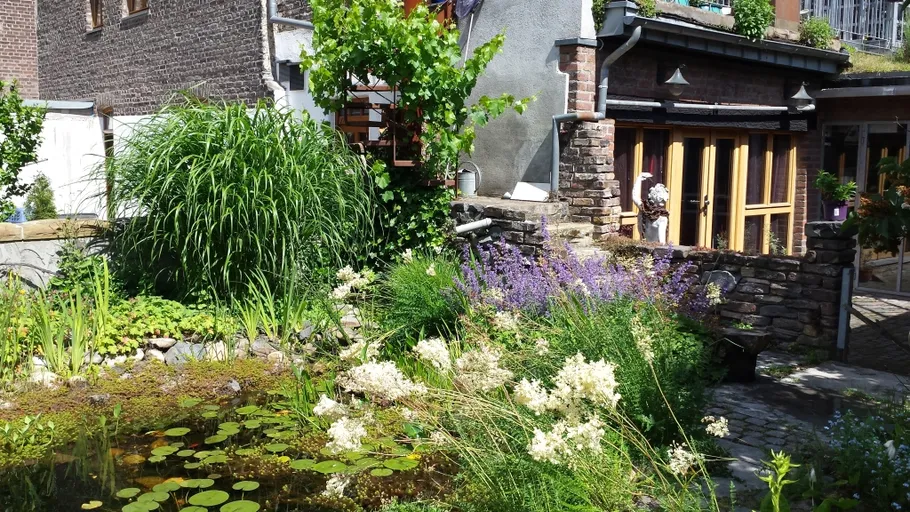 Lush garden with pond beside brick house.