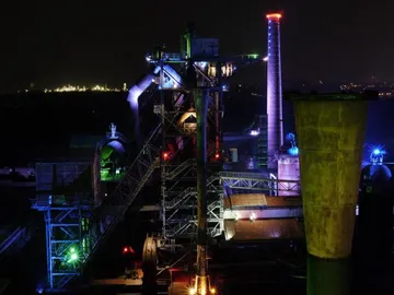 Industrieanlage leuchtet bei Nacht, umgeben von Dunkelheit.