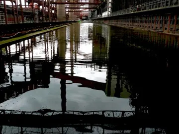 Stilles Wasser reflektiert metallene Strukturen in Industrieumgebung.