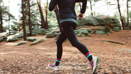 Person running on forest trail, wearing bright socks.