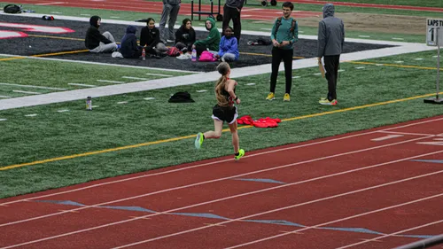 Runner on track with spectators nearby.