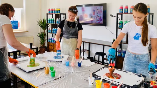 Three women pour paint in art studio.