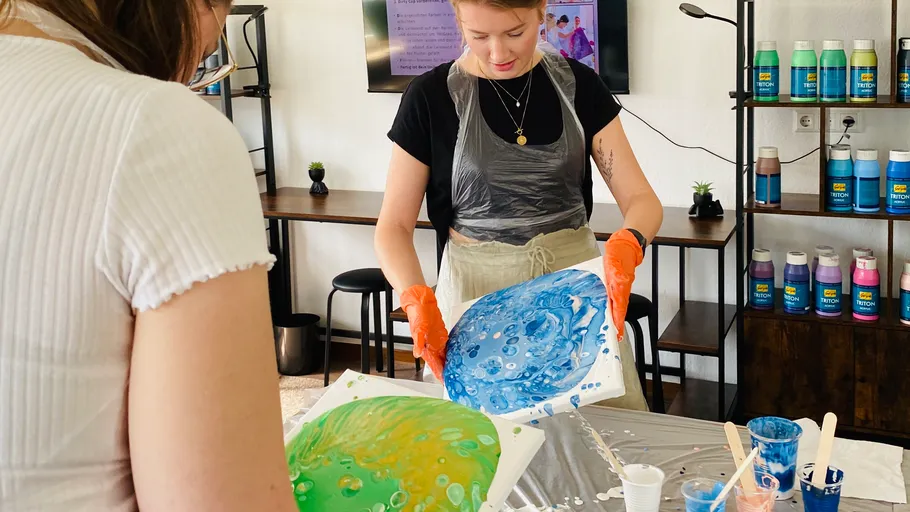 Zwei Frauen gestalten Fluid-Art-Gemälde drinnen.