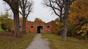 Backsteingebäude mit Torbogen, von Bäumen umgeben.