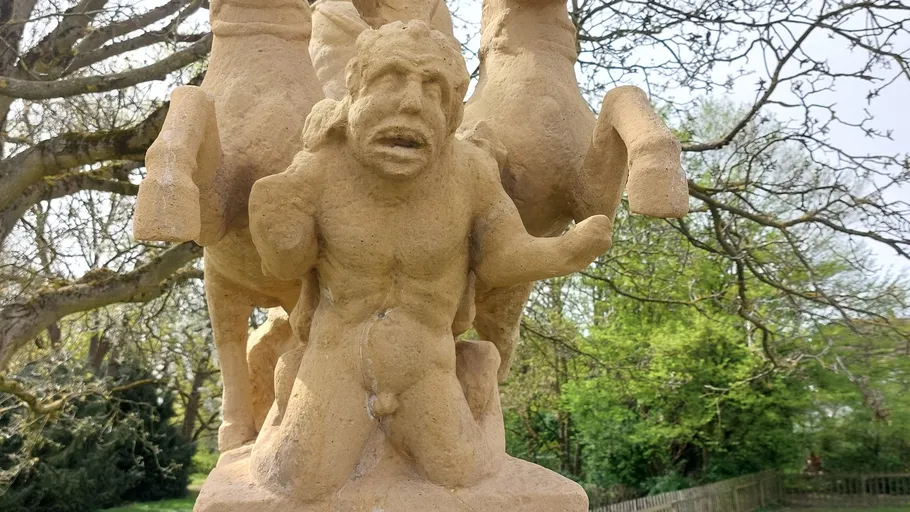 Stone statue of man below horse outdoors.