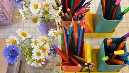Buntstifte und Blumen auf gefliestem Tisch.