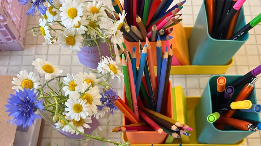 Buntstifte und Blumen auf gefliestem Tisch.