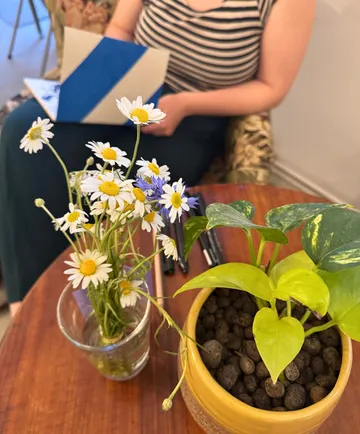 Flowers in vase, plant in pot, person seated.
