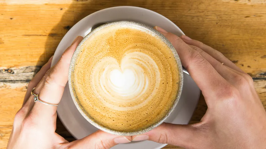 Hände halten Cappuccino mit Herz-Latte-Art.