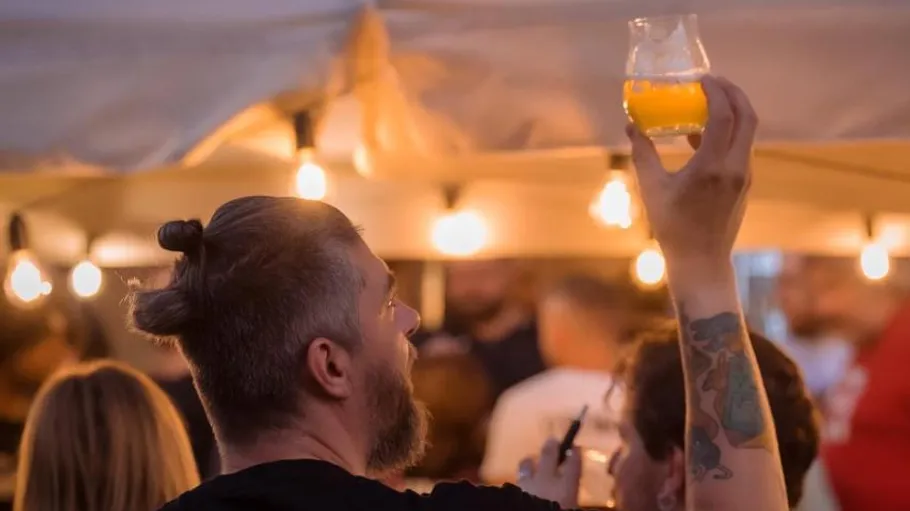 Man holds drink glass at lively outdoor event.