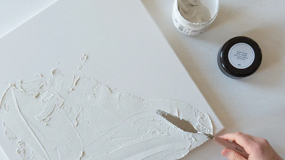 Person applying paste on canvas with spatula.