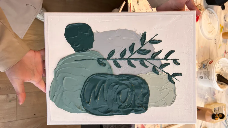 Abstract painting held by hands, on table.