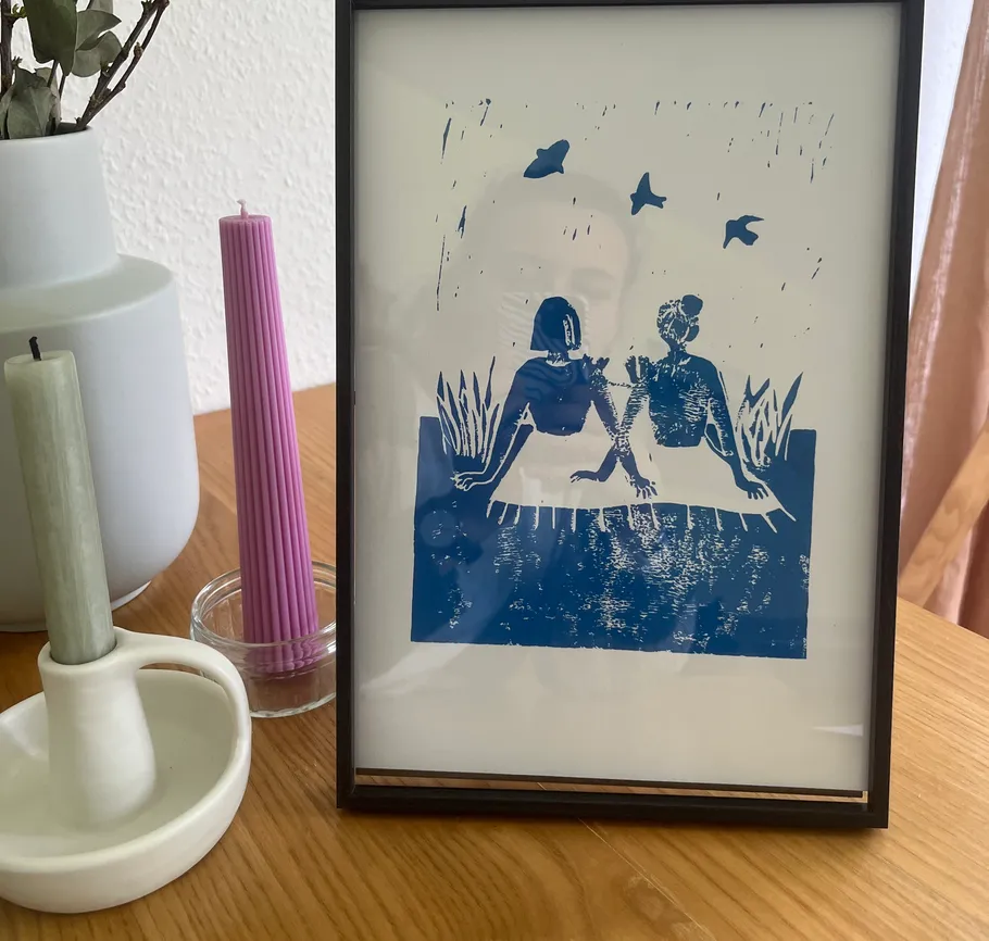Gerahmtes Kunstwerk mit zwei Figuren auf Tisch.
