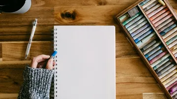Person hält Stift neben leerem Notizbuch.