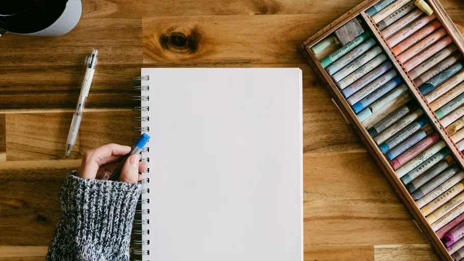 Person hält Stift neben leerem Notizbuch.