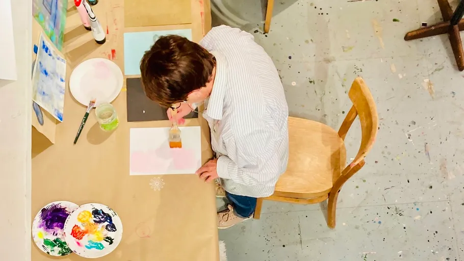 Person painting at table with supplies.