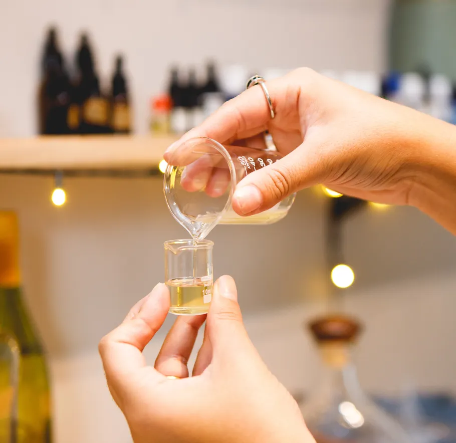 Hands pouring liquid into small beaker, laboratory background.