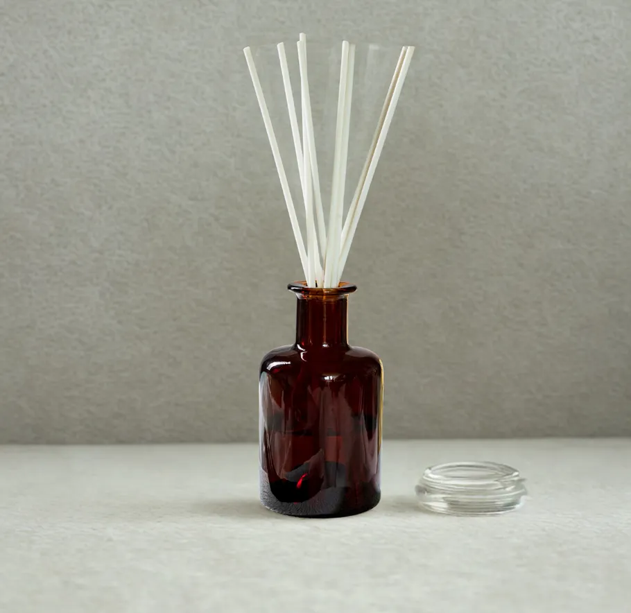 Braune Glas-Diffuserflasche mit Stäbchen, grauer Hintergrund.