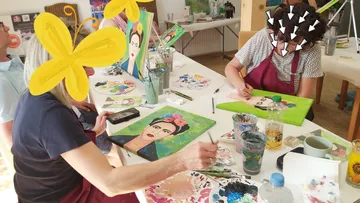 Zwei Frauen malen Frida Kahlo Porträts.