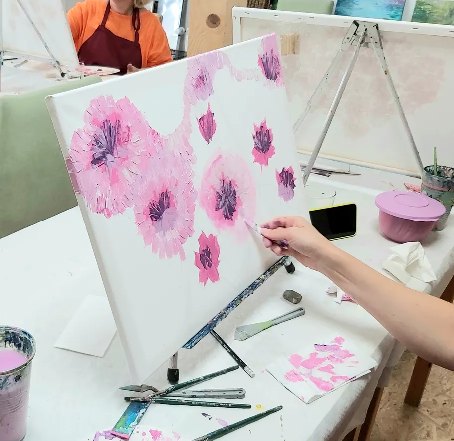 Person painting pink flowers on canvas indoors.