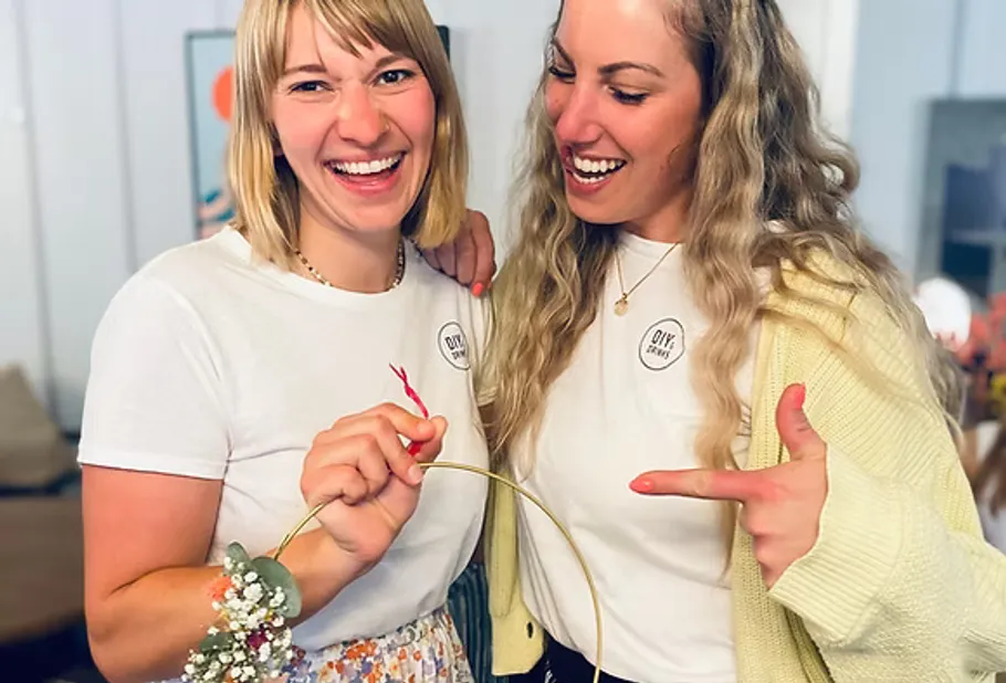 Two women smiling, holding floral wreath indoors.