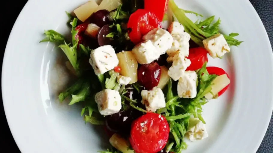 Salat mit Feta, Tomaten und Grünen auf einem Teller.