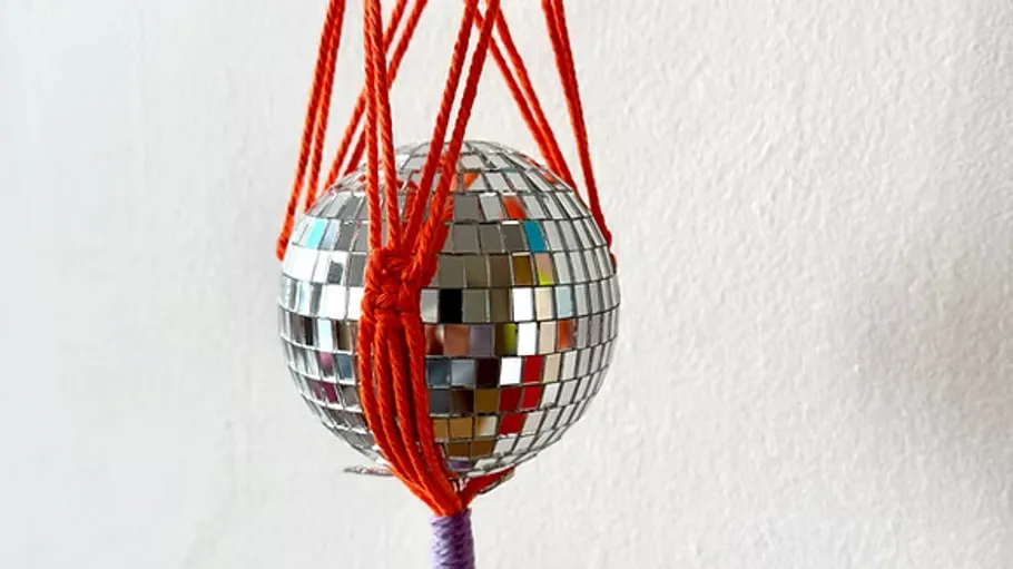 Disco ball suspended by red cords against wall.
