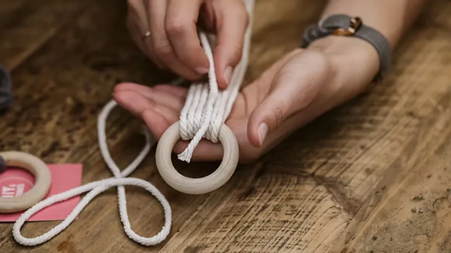 Hands knotting rope through wooden ring.